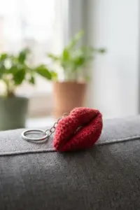 Close-up of dimensional red crochet lips keychain accessory on gray fabric with houseplant